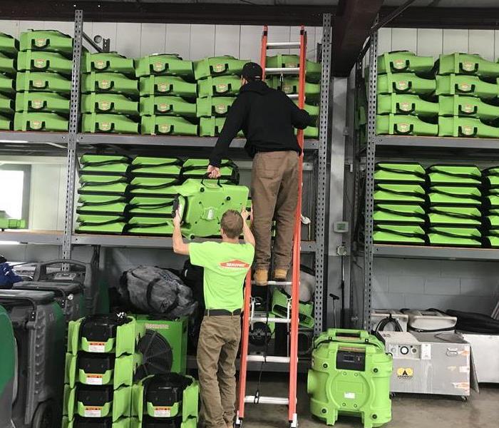 two shelves of equipment with two employees loading a dehum onto the top shelf 