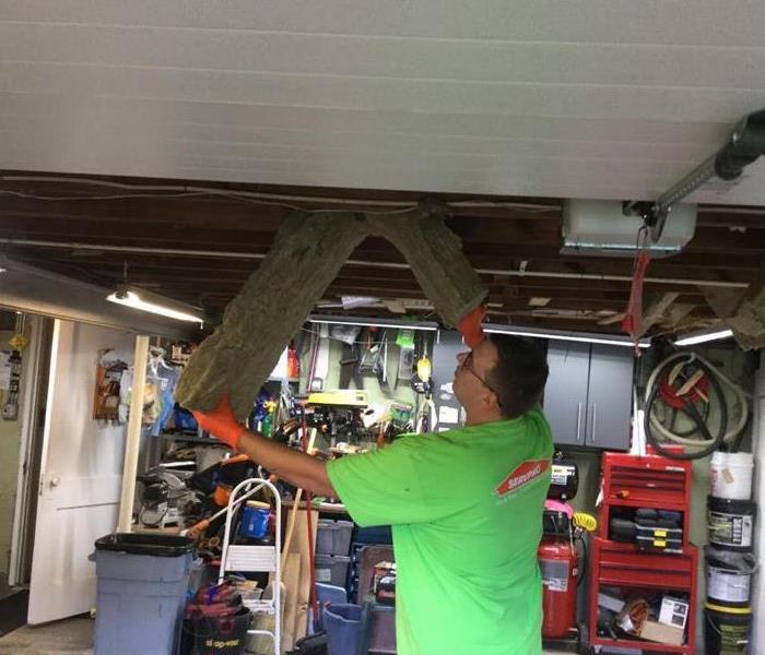 servpro employee ripping drywall out the ceiling of a garage