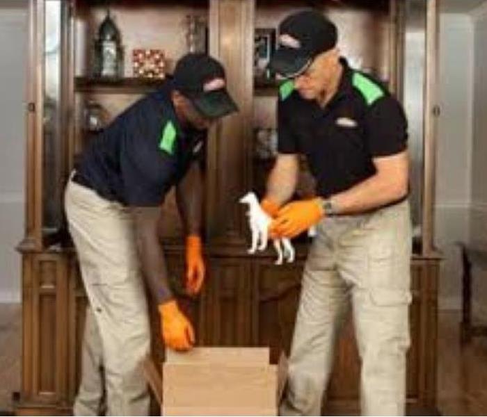 two servpro employees with gloves handling a box in a residence 