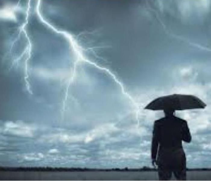 man standing under a umbrella embracing for an impending storm. sky full of rain and lightning