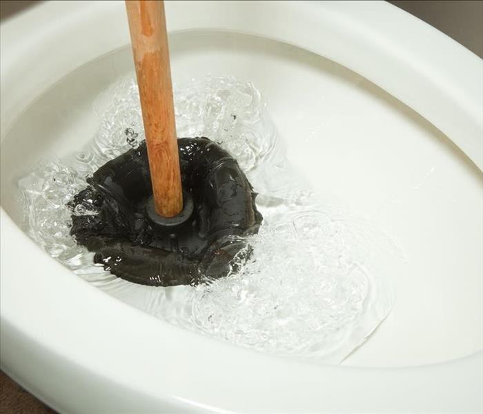 image of person using a plunger to unclog a clogged toilet